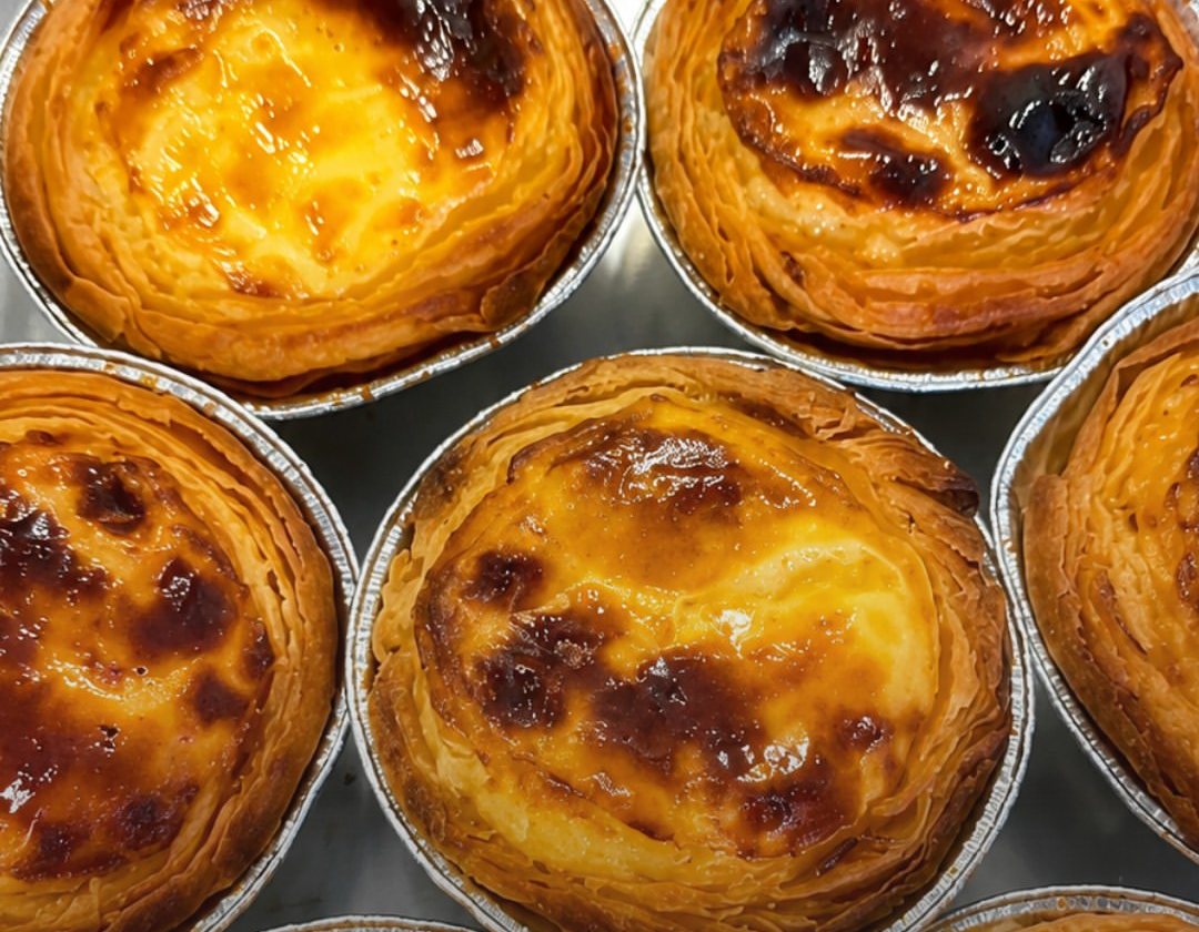 Vários pastéis de nata acabados de cozer em formas de alumínio, vistos de cima