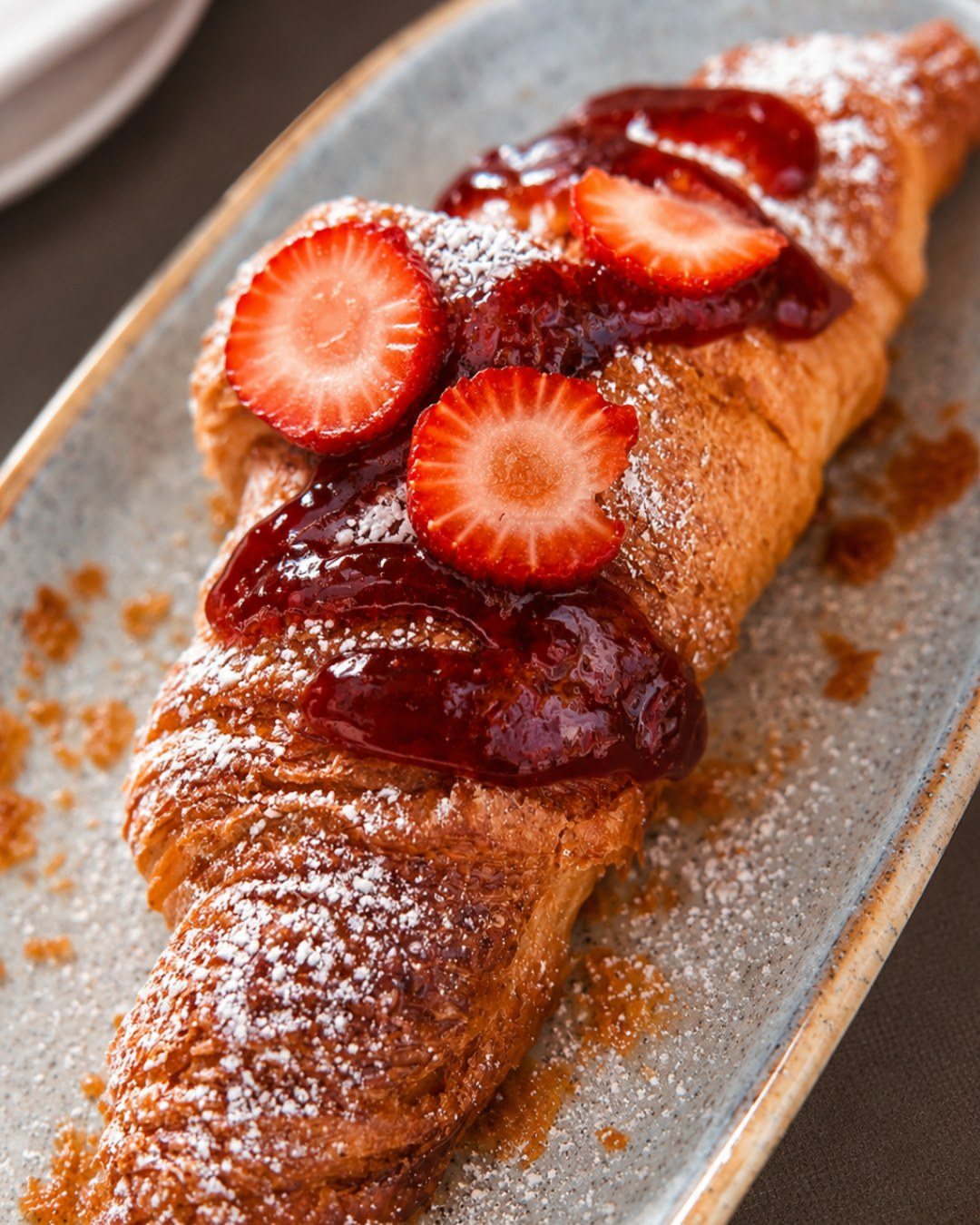 Croissant com morangos, doce de morango e açúcar em pó num prato comprido azul-acinzentado